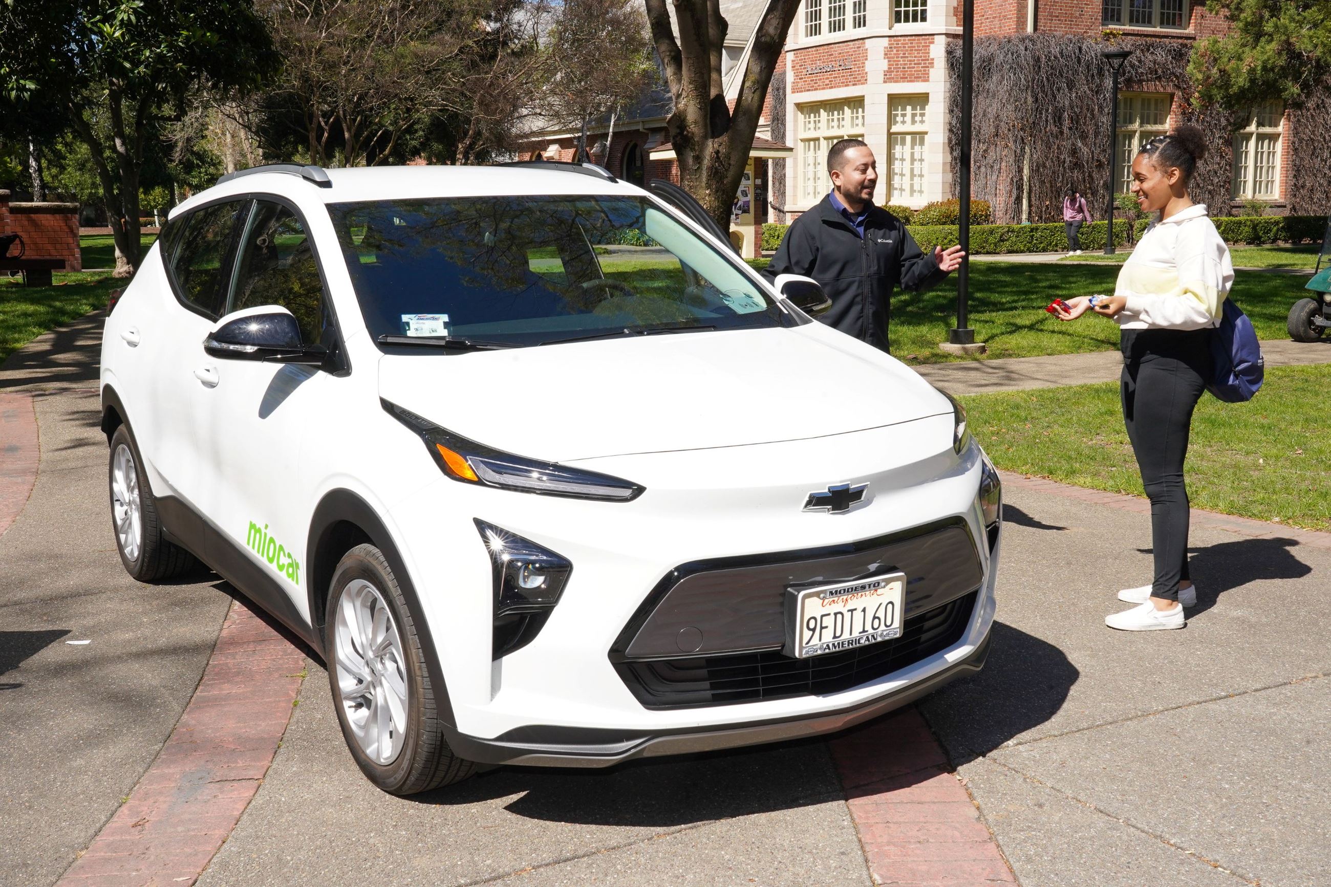 Two people stand beside a Míocar vehicle discussing the carshare service.